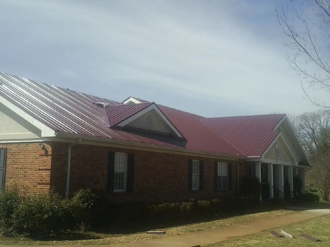 Red metal roof with gabled entries on a long brick building, from a Hail Damage Roof Repair job in Carpenter
