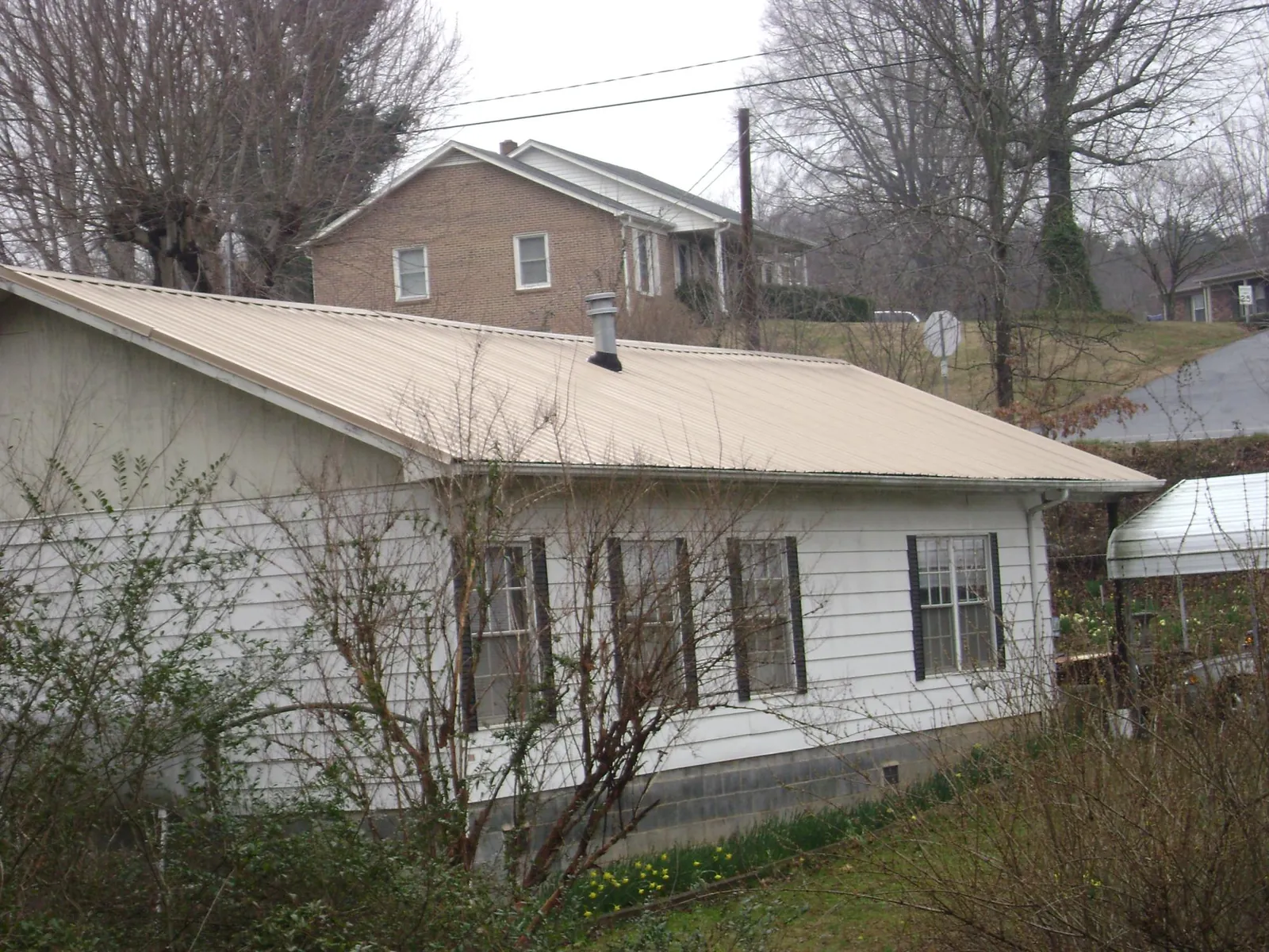 Tan metal roof on a white sided house set into a hillside — Commercial Roofing by Roofing Brothers in Carpenter
